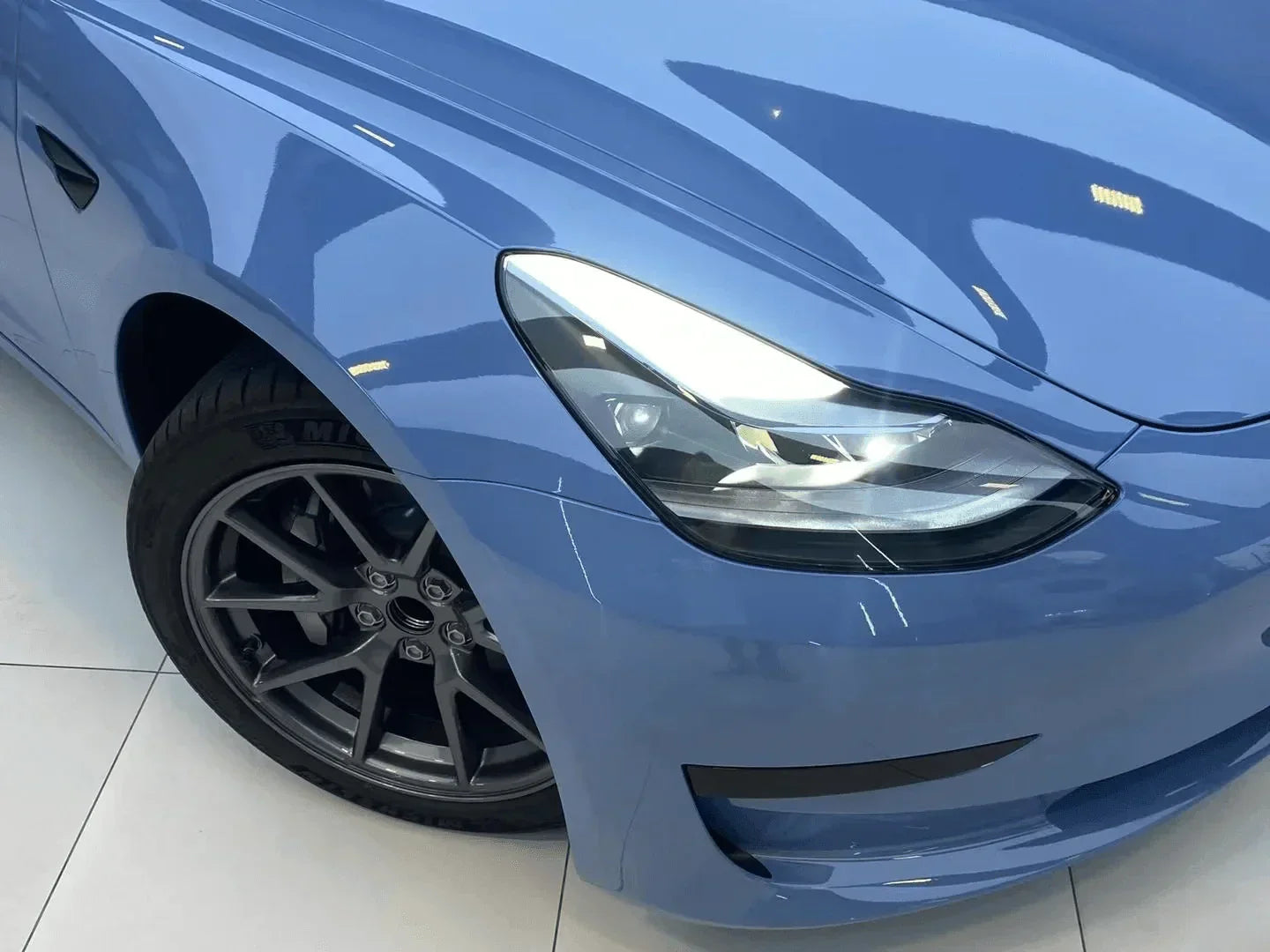 Close-up of a blue car's headlight and front wheel on a white background