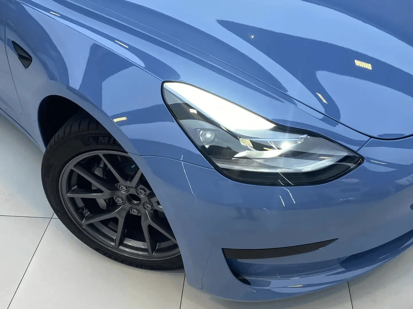 Close-up of a blue car's headlight and front wheel on a white background