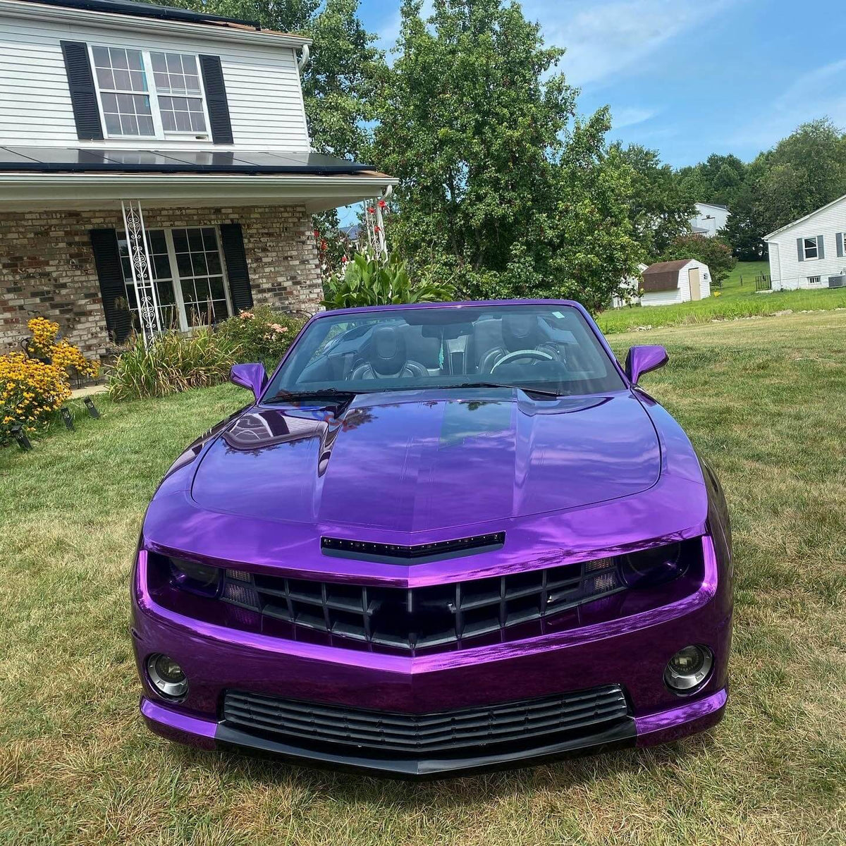 Purple convertible car parked on grass with a house and trees in the background